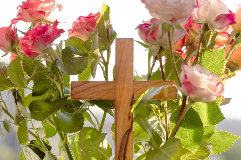 Cruz de madera con rosas rosadas bajo la luz del sol